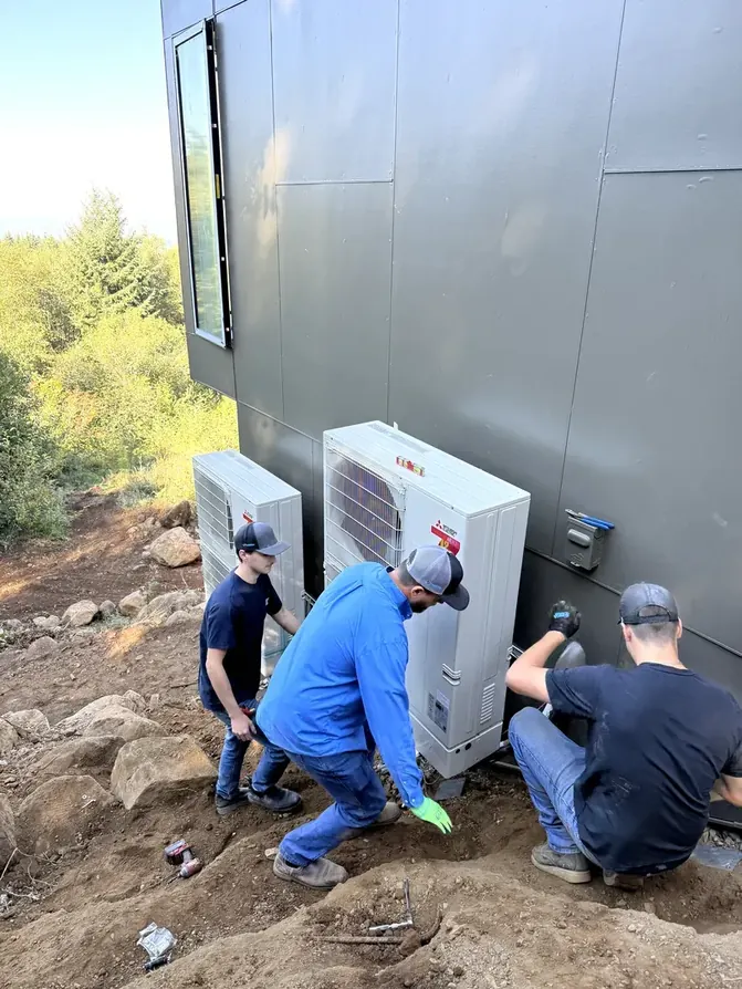 All Around Mechanical technicians installing a ductless heat pump on the side of a home